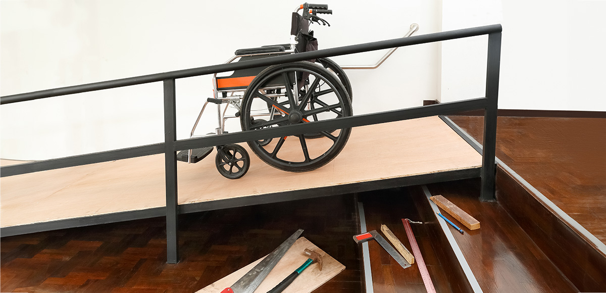 Rullstol står på en nybyggd ramp intill en trappa inomhus. Foto.