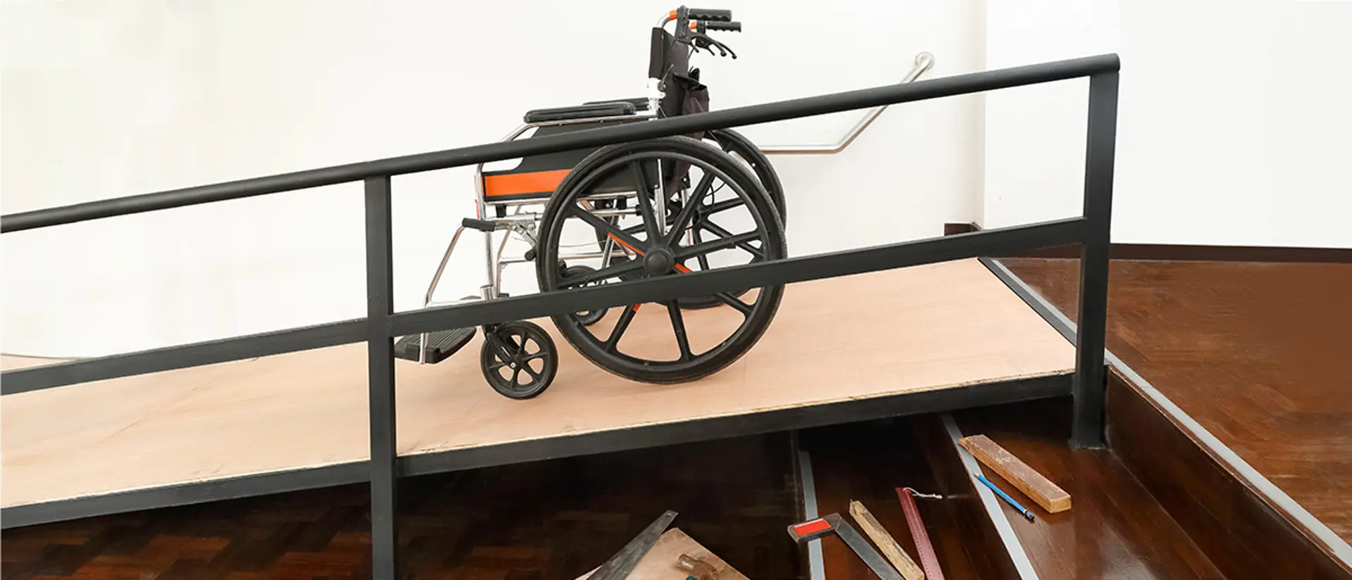 Rullstol står på en nybyggd ramp intill en trappa inomhus. Foto.