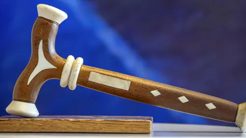 En ordförandeklubba av trä och horn mot en blå bakgrund. Foto.